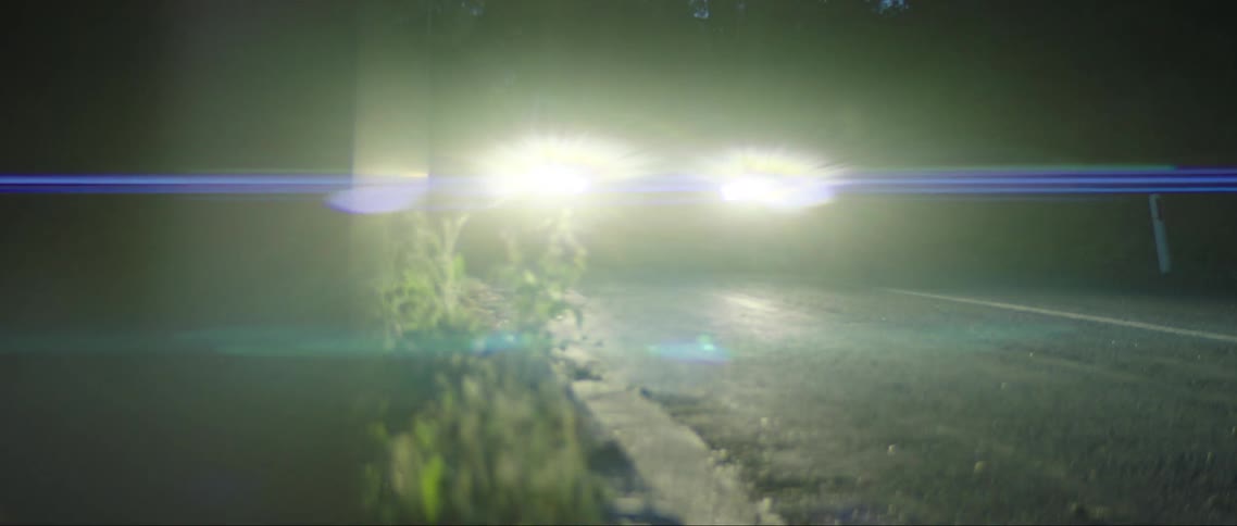 A car with bright headlights drives down a road
