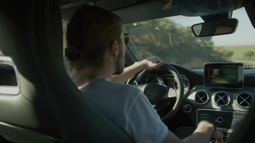 A young man drives a car through the countryside