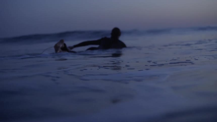 A surfer swimming in the ocean at dusk