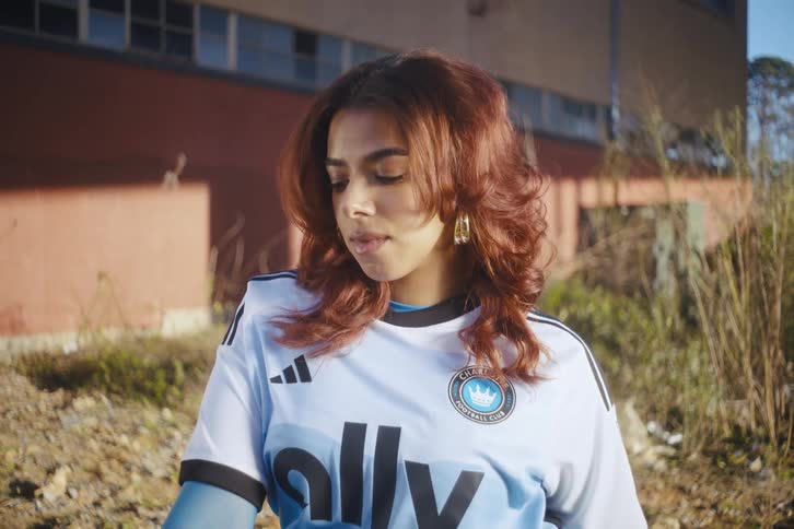 Model sitting on a chair outdoors with abandoned buildings around posing with a football team shirt sponsored by adidas