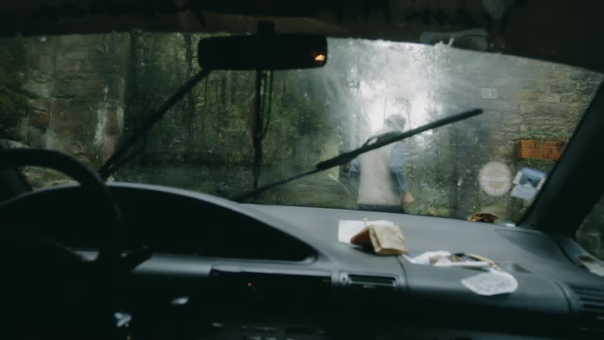 A man walks in front of a car through a concrete entrance to a forest