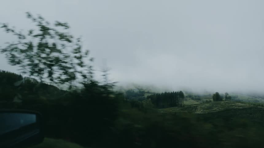 A view of the countryside under a thick layer of clouds seen from a moving vehicle