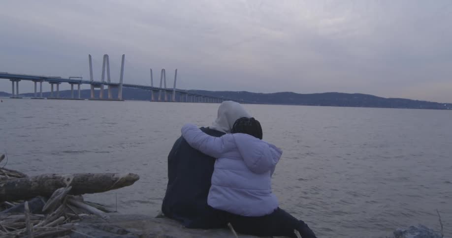 Vision of a couple holding each other while sitting on a rock by the sea on a cloudy morning
