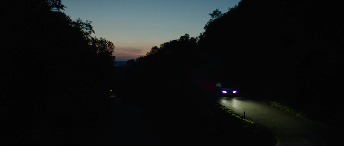 A car driving on a road through the countryside at nightfall