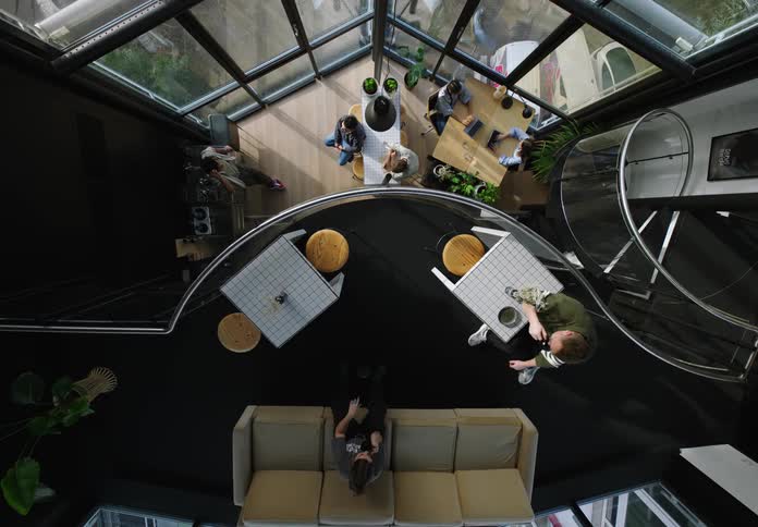 Three people in a loft walk downstairs to join the others who are sitting
