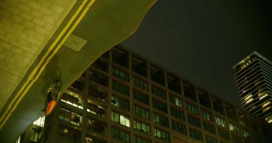 Reflection of a person riding a bicycle on a facade in the city at night