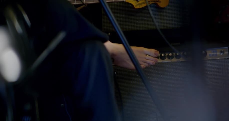A musician sitting down barefoot with legs crossed while holding a bass guitar