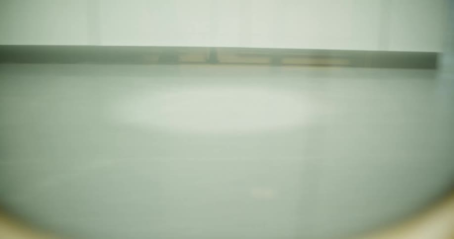 Close up of a window of an indoor train passing through a moving station with a reflection of peoples legs