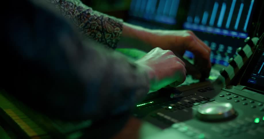 Hands move sliders on a recording studio mixing desk
