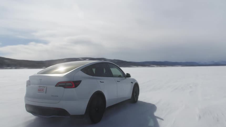 Tesla sedan car at high speed on a snowcovered terrain with mountains around