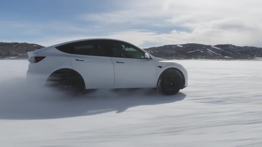 White tesla sports vehicle speeding on snowcovered terrain in nature with mountains on the horizon