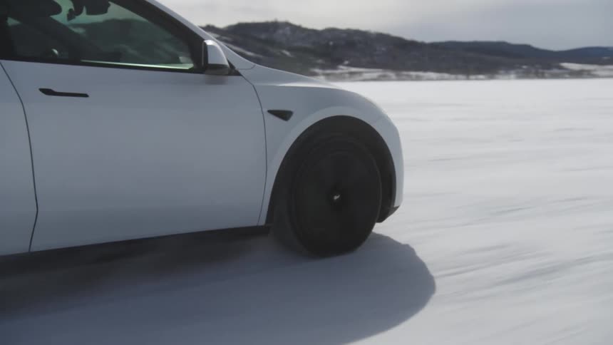 White tesla car speeding through snowcovered terrain with mountains on the horizon