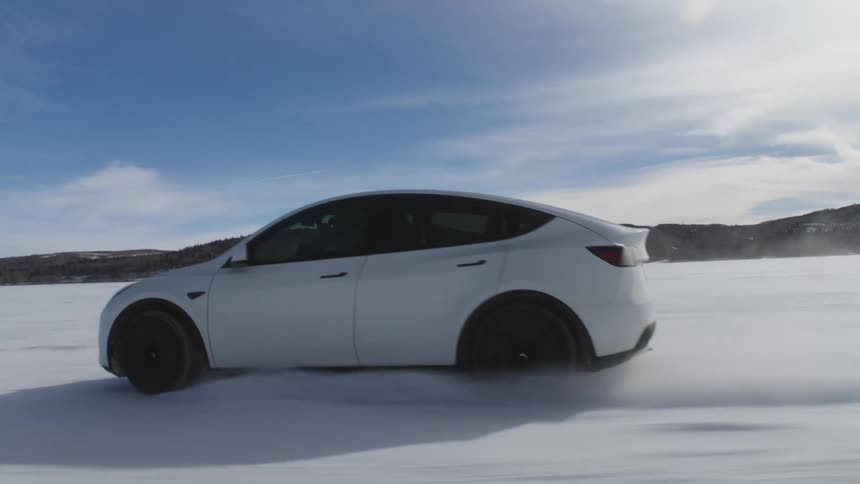 A white tesla model 3 car is driving on a snowcovered landscape
