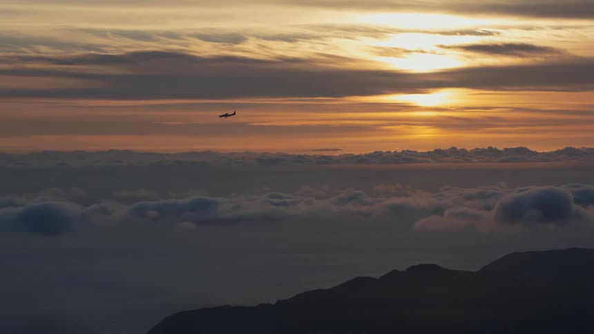 A small private plane flying over the sky that has several clouds and a sun in the morning