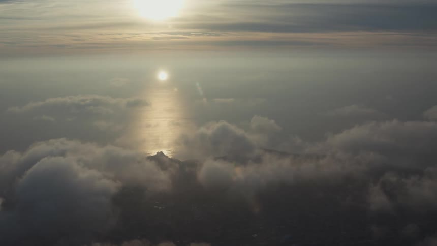 Aerial scenery above cloud level overlooking an island in the ocean with sunrise on the horizon