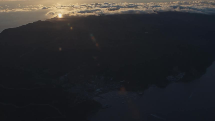 An aerial view of a large island facing the sea and the sky is full of clouds and flares of sunlight