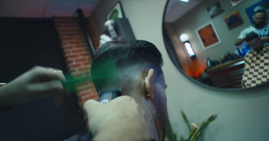 Barber cuts hair of customer sitting in front of round wall mirror