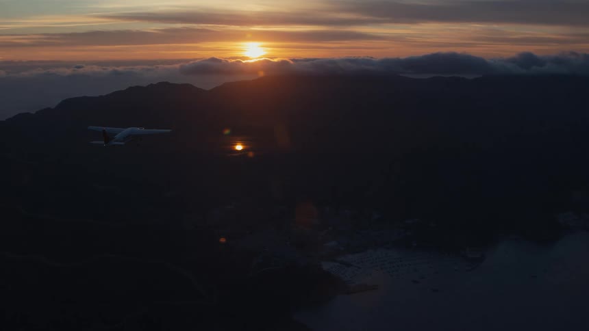 Aerial panorama of a small plane flying over a mountainous island with a sunset on the horizon