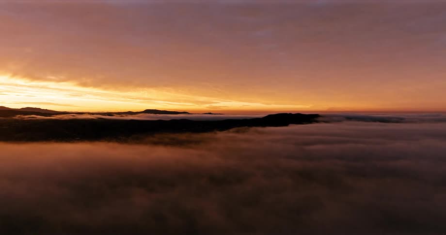 Aerial scenery of a landscape with silhouette of mountains with mist in a purple dawn sky
