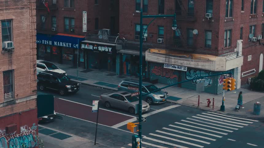 A street with the traffic lights closed and cars stopped and there are several large buildings around and people crossing the pedestrian crossing