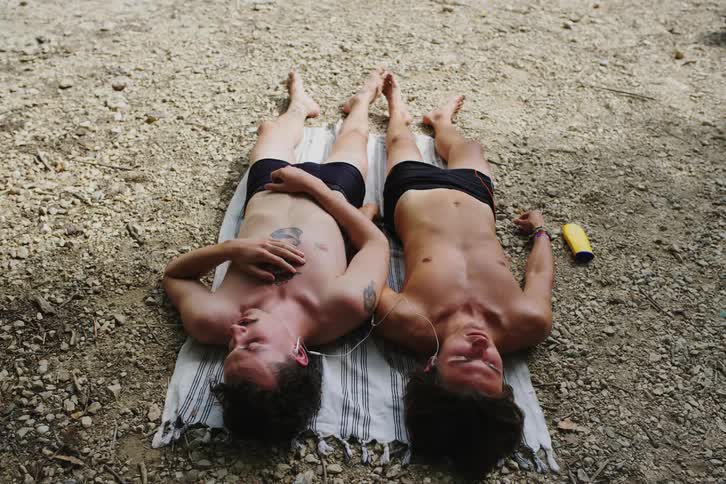 Two teenage boys lying in the sun sharing a beach towel