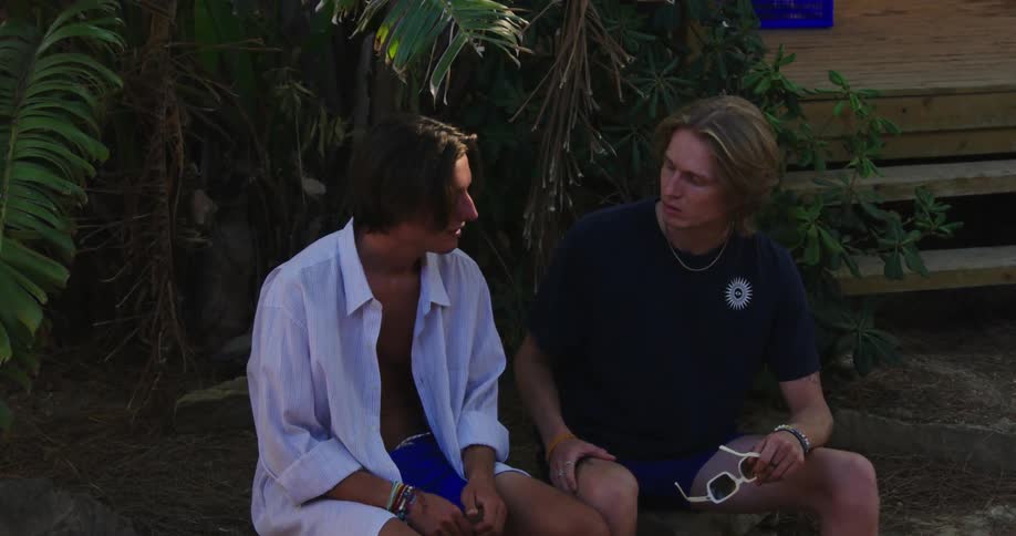 Two young man in summer clothes sitting and talking in front of a wooden porch