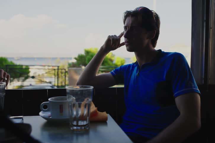 Some men are gathered around a table and are talking and one of them is smoking