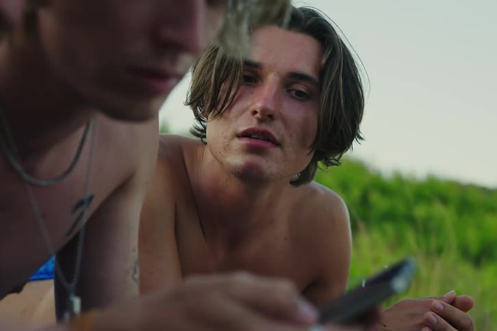 Man sunbathing with friends looks over to see what his friend is doing on smartphone