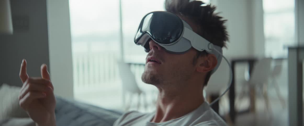 A man sits on a couch as he plays around with virtual reality goggles