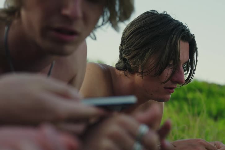 Portrait of three young men without shirts in a natural environment talking and using their cell phones