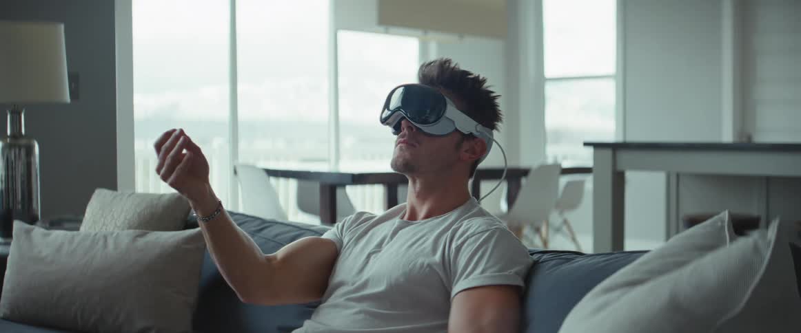 A man sitting on a couch uses virtual reality goggles