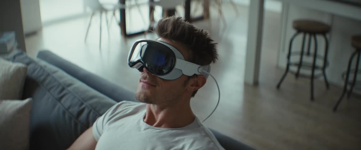 Man sitting in living room turns his head interfacing with the virtual reality headset he is wearing