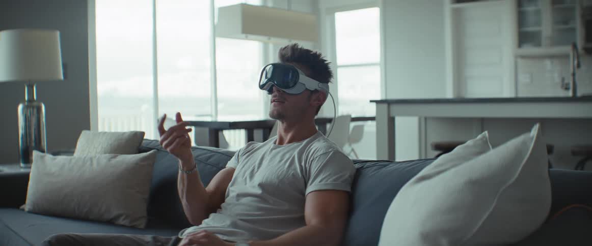 A man is sitting on the couch using a virtual reality headset