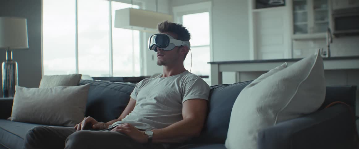 A man is sitting on a sofa while he has a vr glasses on his face and he is smiling