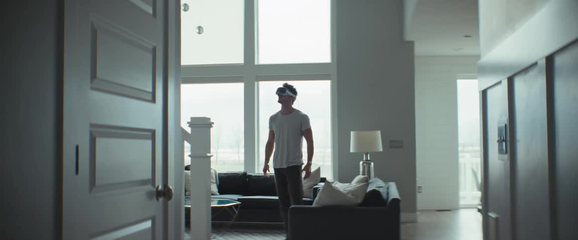 A man is standing in an allwhite living room and is wearing virtual reality glasses