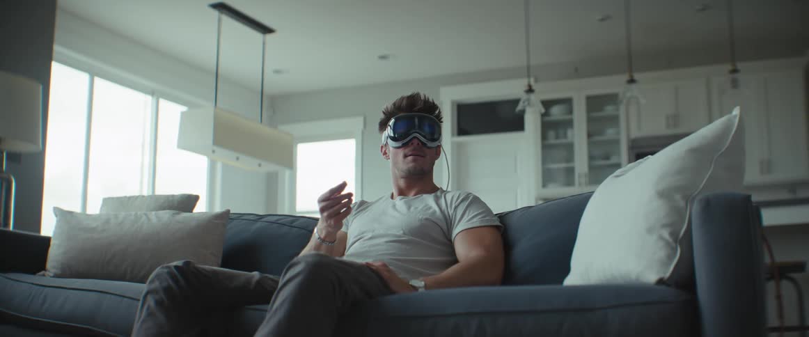 Man sitting in living room smiles while interfacing with virtual reality headset