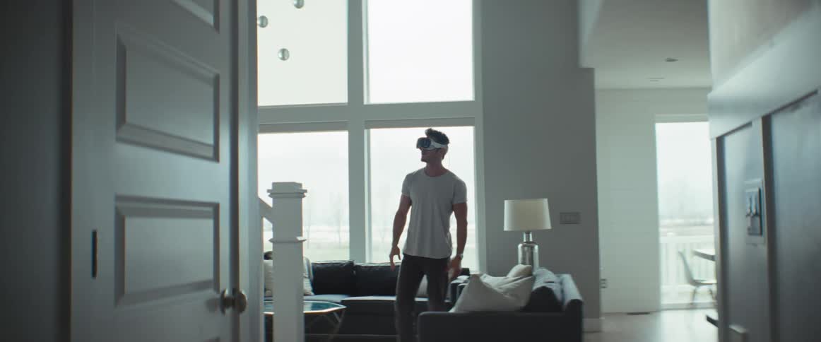 A man stands in a living room while using virtual reality goggles
