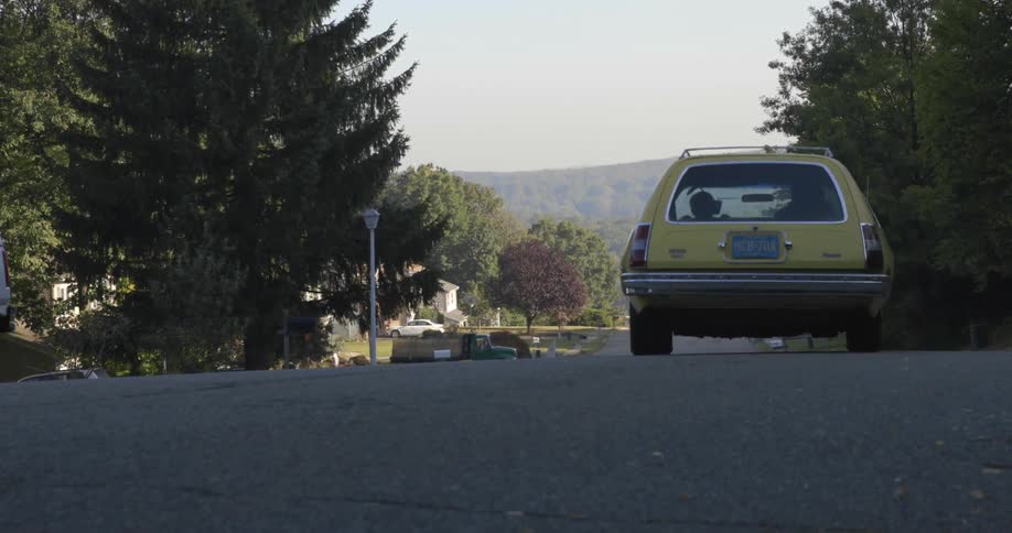 A yellow car drives down a neighborhood street