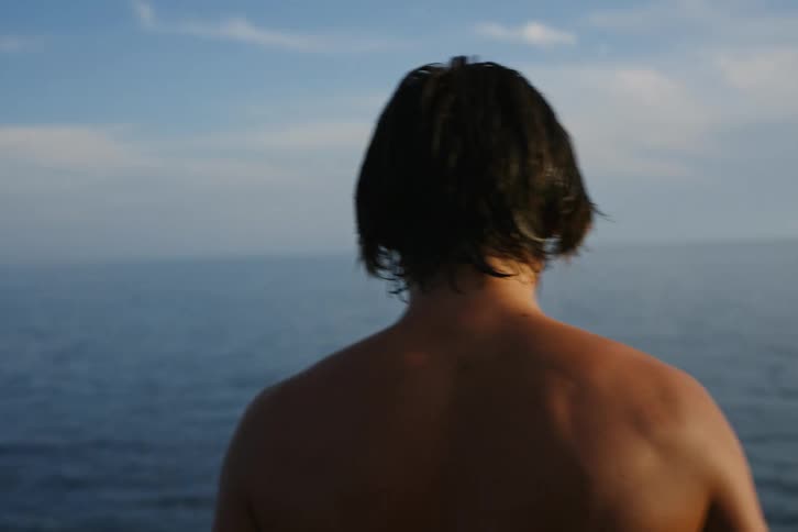 Shirtless man jumps into the ocean on a cloudy day