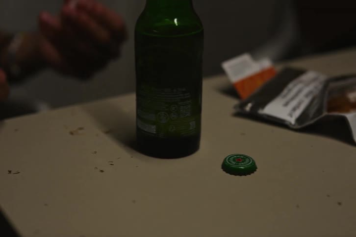 Young man next to his friends preparing a cigarette while standing at a table with drinks and talking