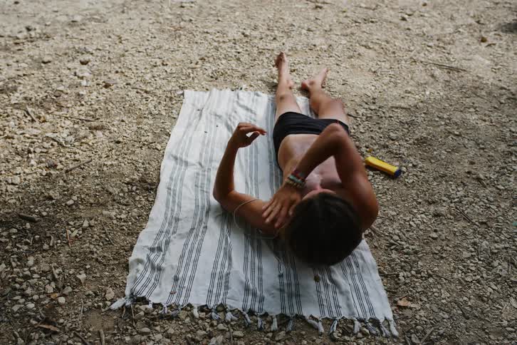 Young man lying on a towel taking sunscreen and applying it to the upper part of his body