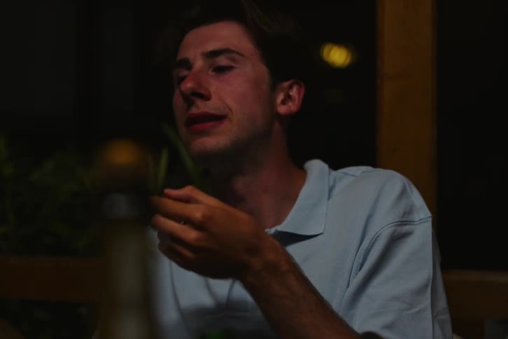 Three young men are standing next to each other and talking and one of them is smoking and there are several drinks on the table in front of them
