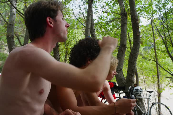 Three friends sitting in a forest without shirts eating and talking