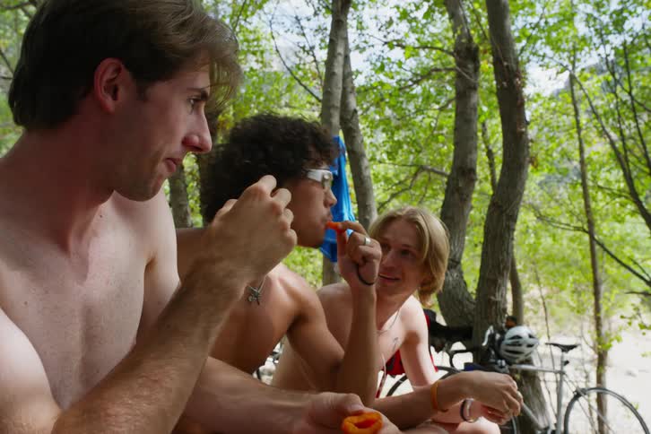 Three young men in the woods wearing only their underwear eating fruit then throwing the pits at a fourth