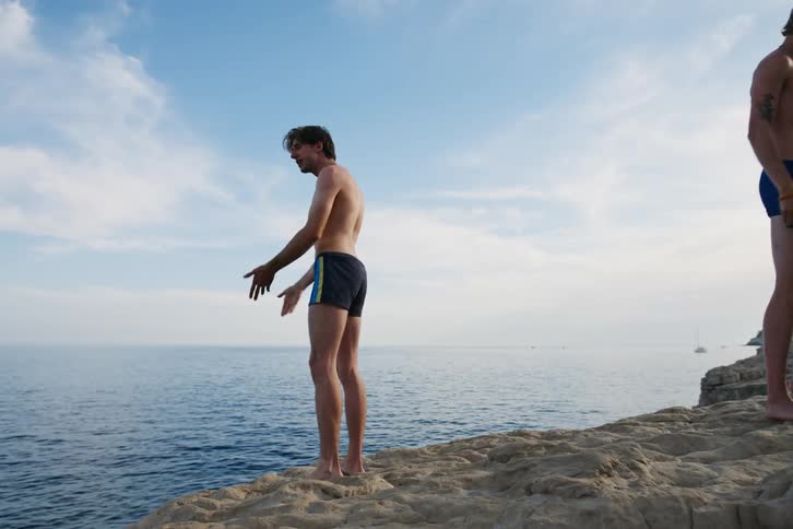 Five boys are hugged in a circle and walk over a rock to look at the sea