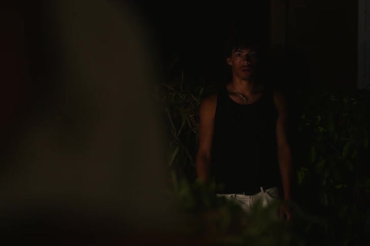 A young man walking in the dark stops and looks at something that surprises him before continuing on