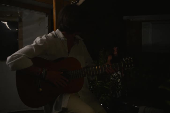 A woman sits in the darkness while playing an acoustic guitar