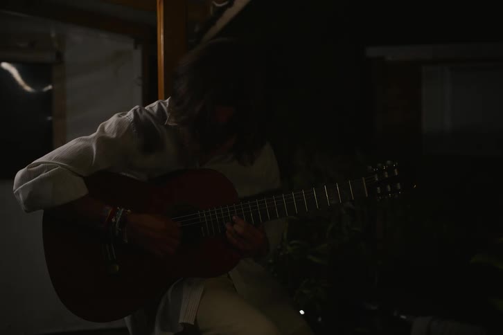 Man plays guitar while sitting near building at night