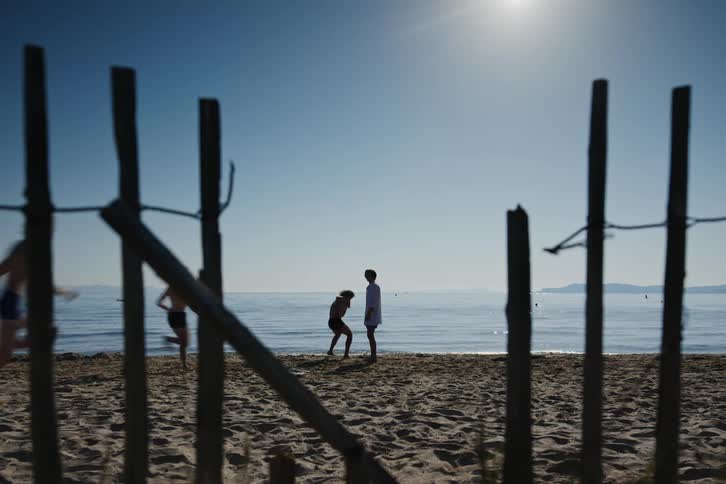 Two men face to face and then other friends arrive and start playing while they are in the sand by the sea