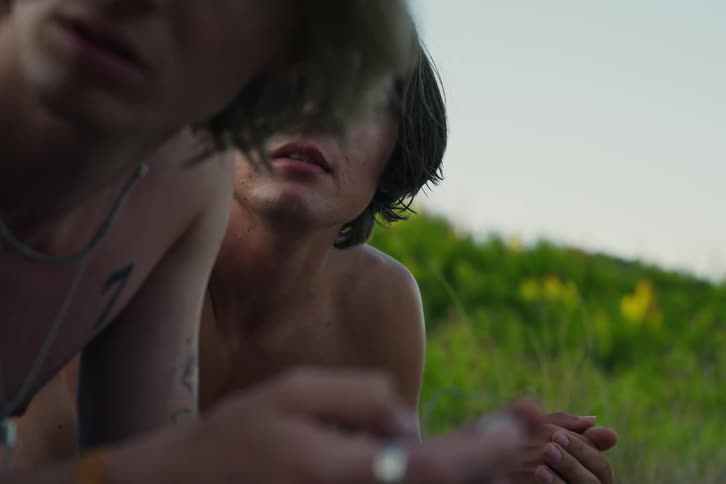 Portrait of two shirtless friends lying in a natural environment with one of them watching what his friend is doing on his cell phone